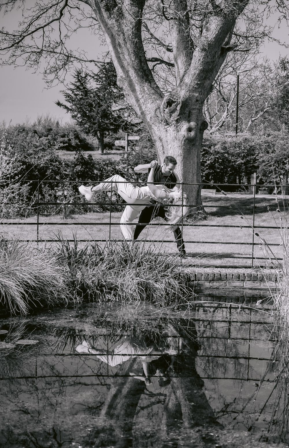 Black and white photo of someone sitting in a tree above a reflective pond.