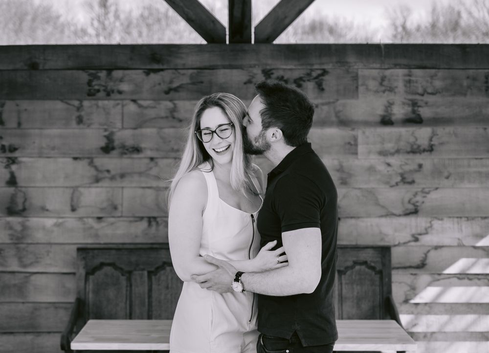Black and white portrait of couple sharing intimate moment against rustic wooden wall.