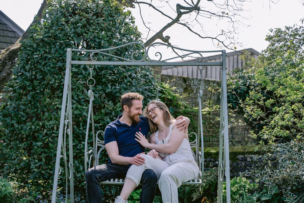 A couple shares a tender moment while sitting on a garden swing surrounded by greenery.
