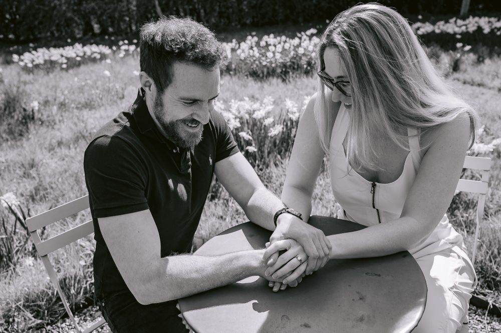 Black and white photo of couple holding hands while seated outdoors.