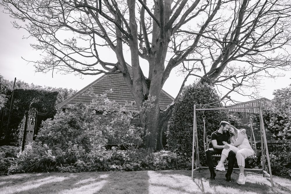 Black and white photo of people sitting together on an outdoor swing in a garden setting.