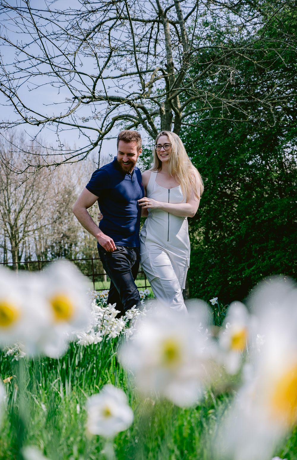 Spring engagement photo with couple among blooming daffodils in garden setting.