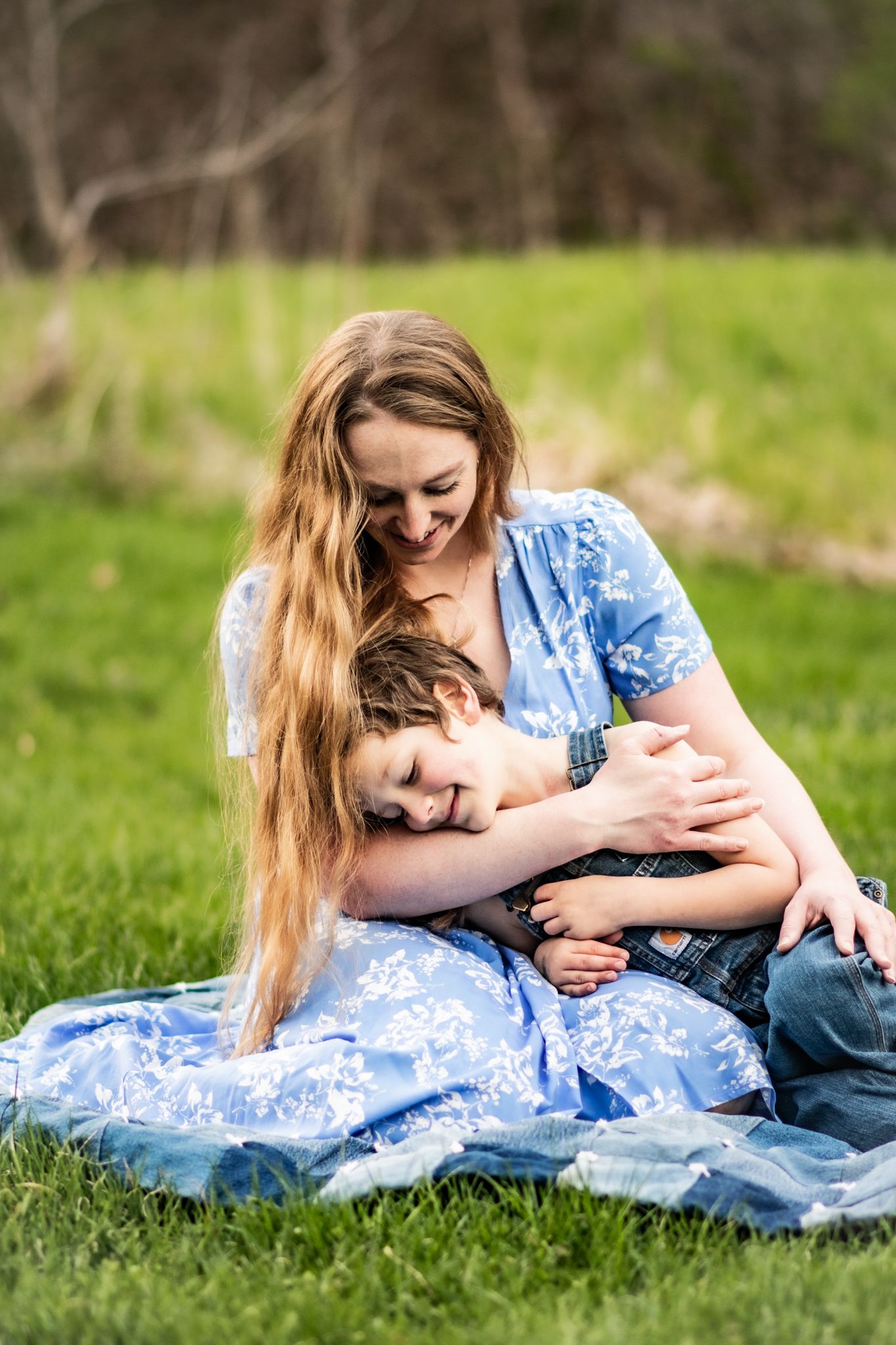 A tender moment captured on grass as a parent embraces a child in a blue dress.