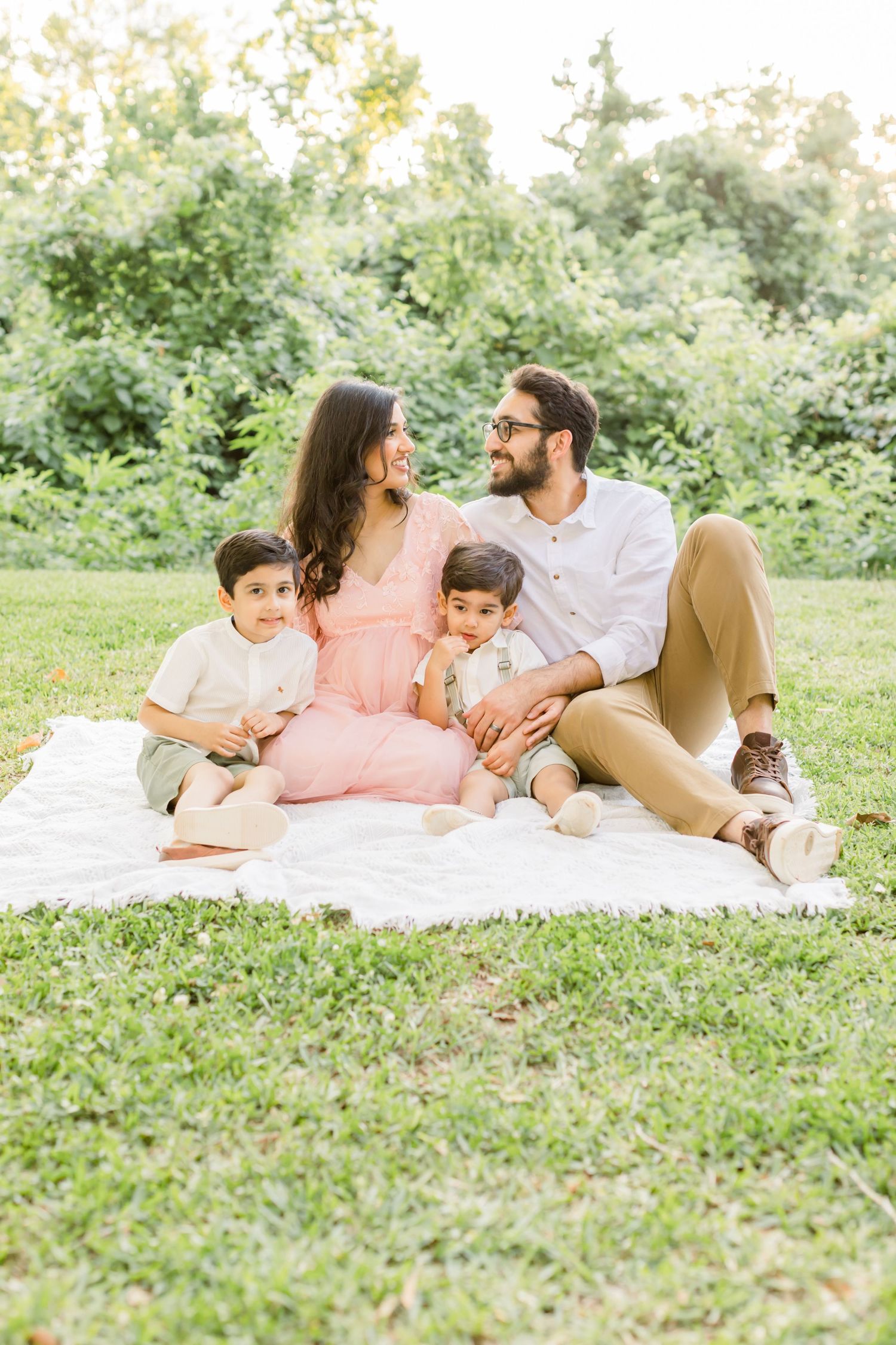 A family relaxes together on a white blanket during an outdoor photo session.