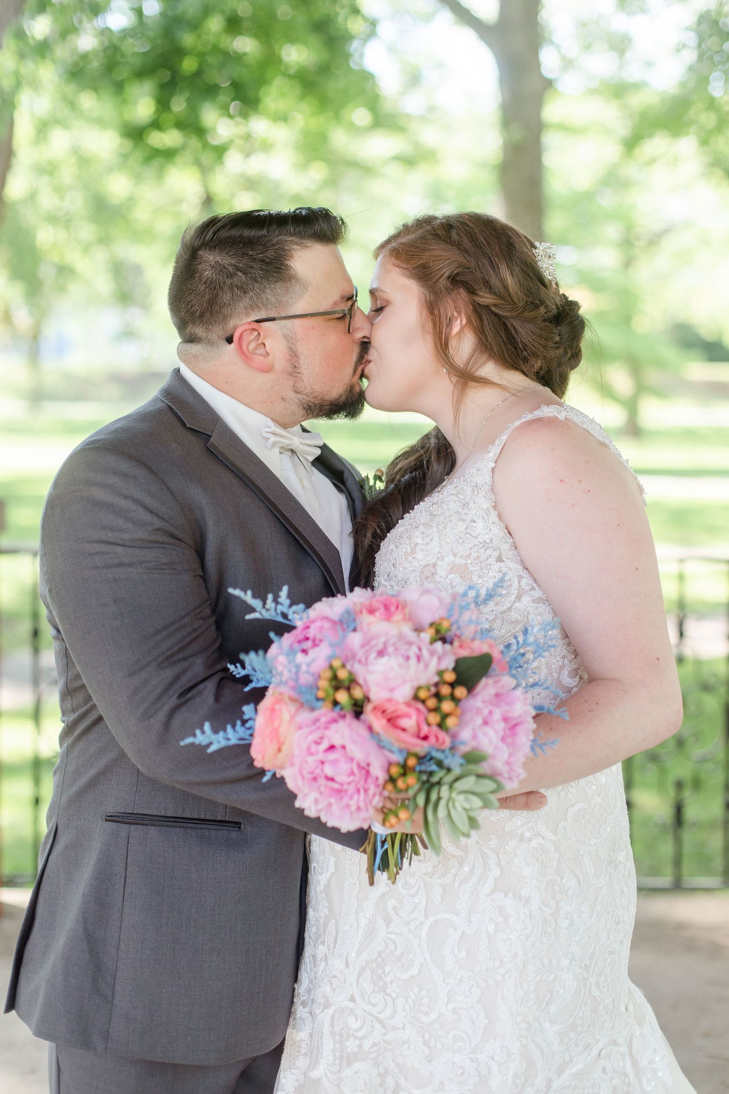 Couple shares romantic moment with pink floral bouquet during outdoor wedding photoshoot.