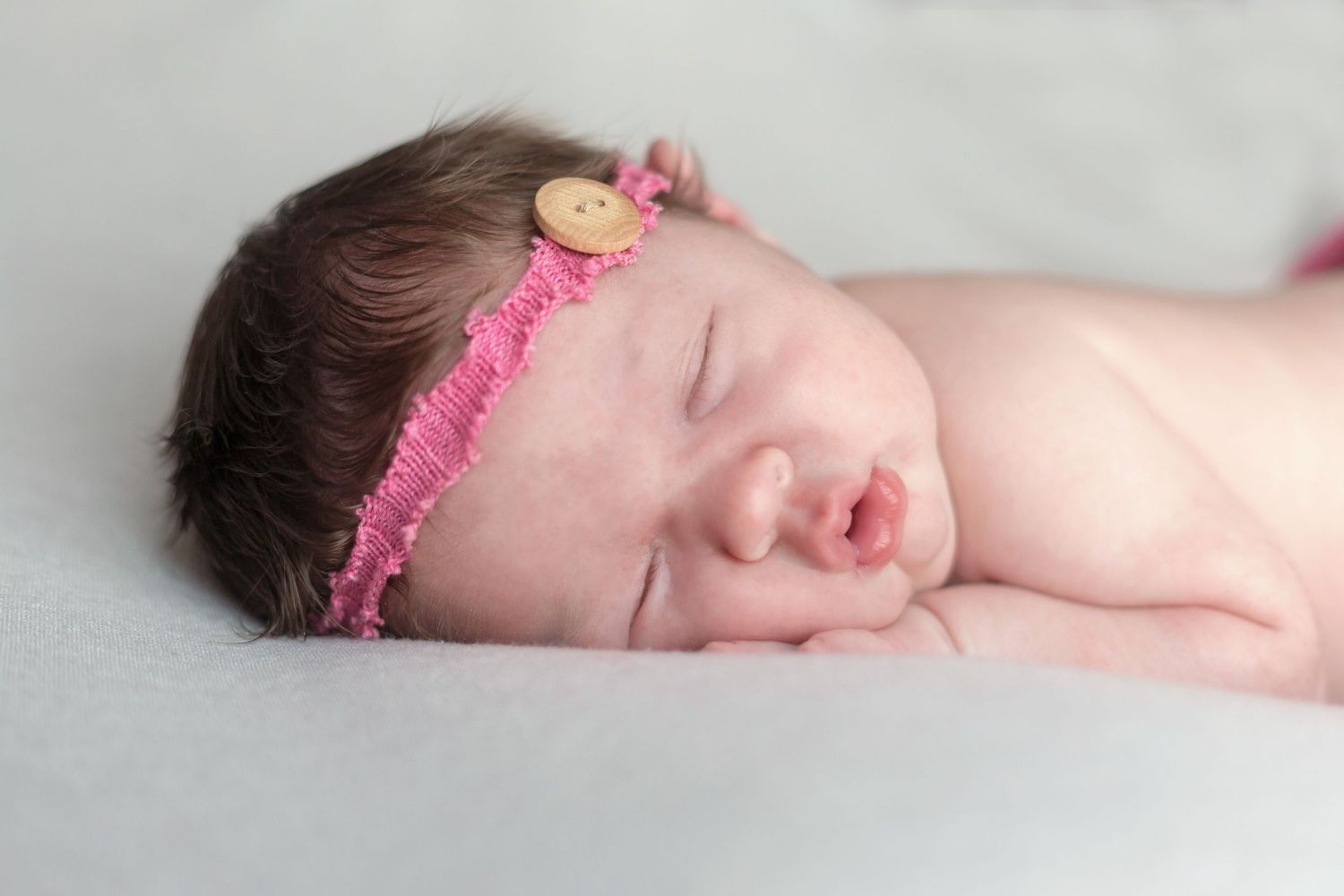 Sleeping newborn wearing pink headband on white background.