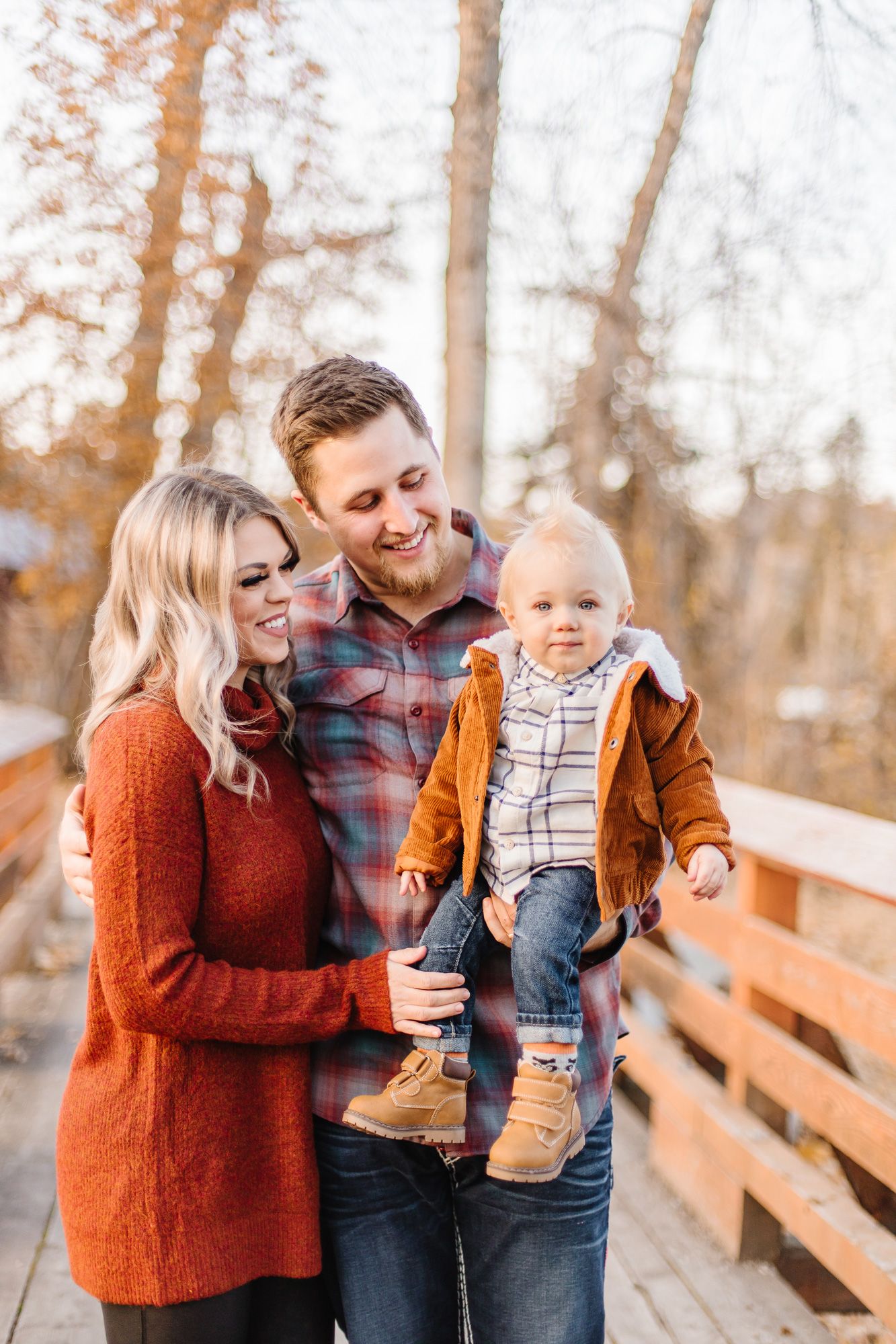 Family shares joyful moments on wooden bridge during autumn photo session.