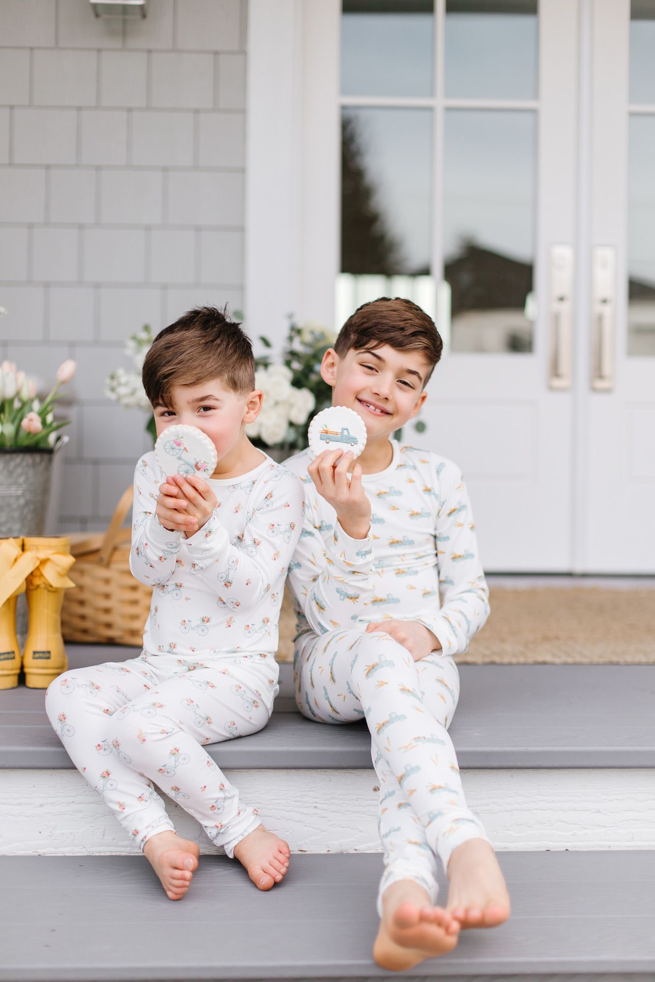 Two children in matching white pajamas sit and play on gray steps.