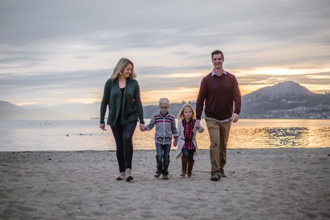 A family walks along a scenic beach at sunset with mountains in the background.