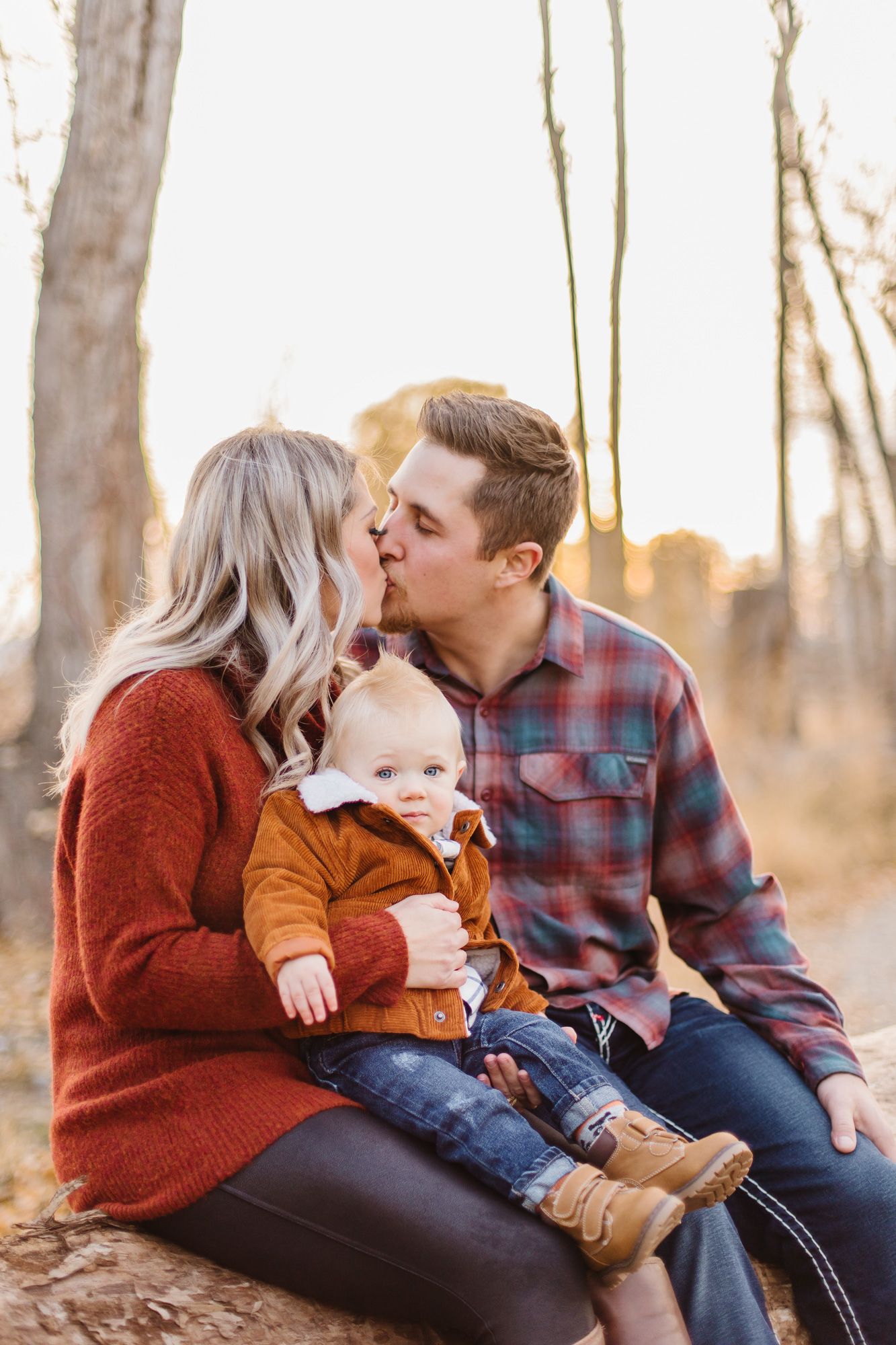 A tender family moment captured outdoors at sunset among autumn trees.