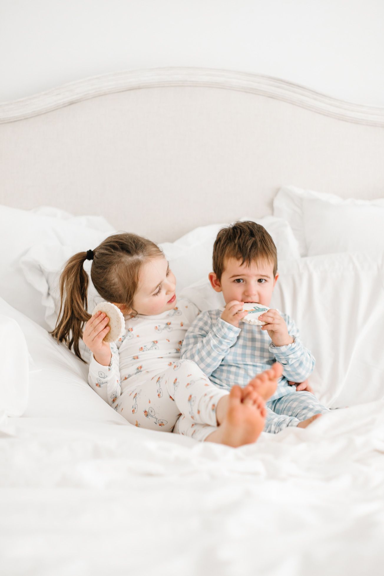 Two children in sleepwear relaxing on a white couch together.