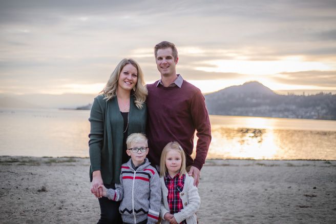 A family stands together on a beach at sunset with mountains in the distance.