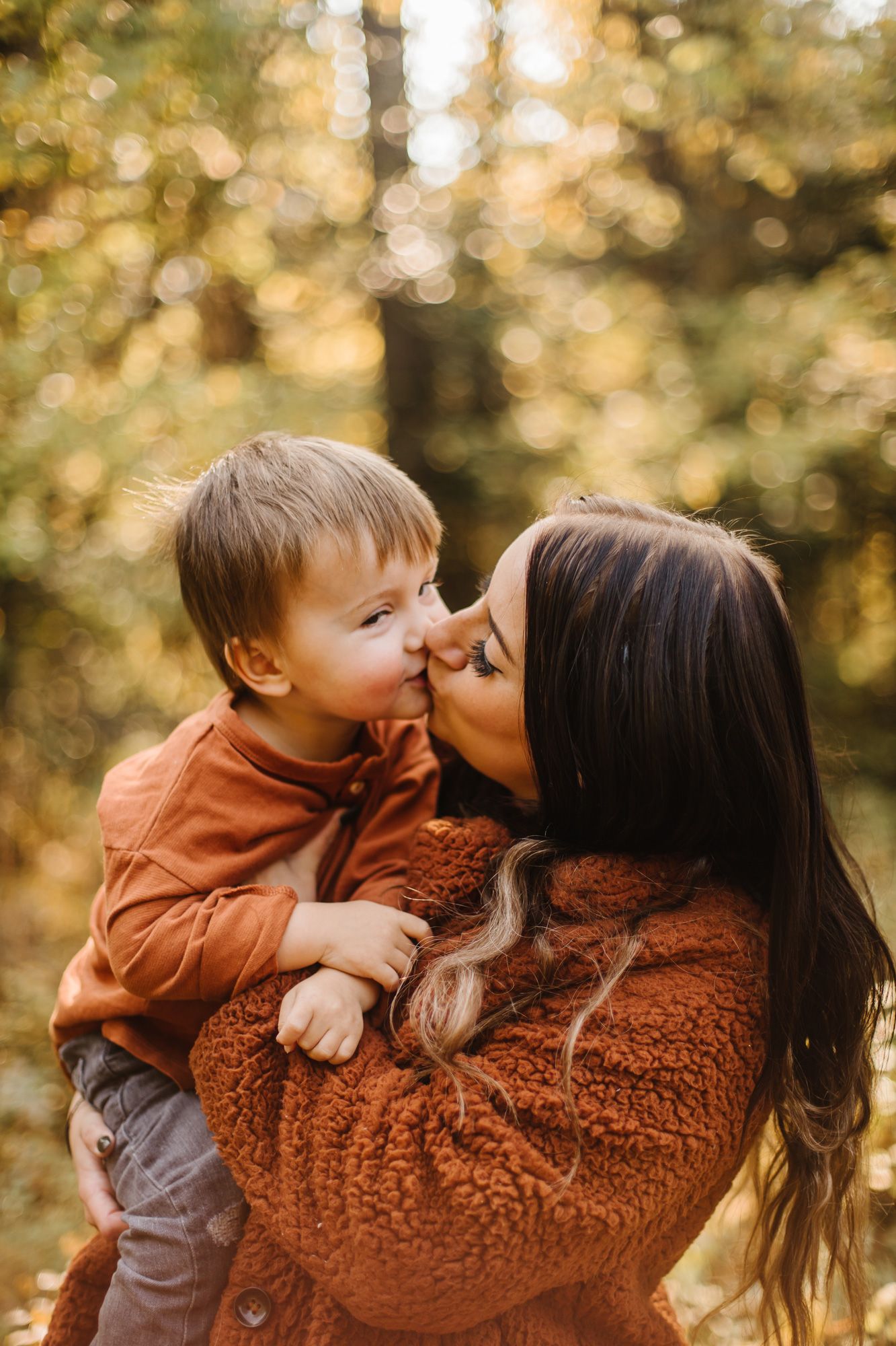 Tender moment captured between two people wearing brown sweaters against autumn foliage.