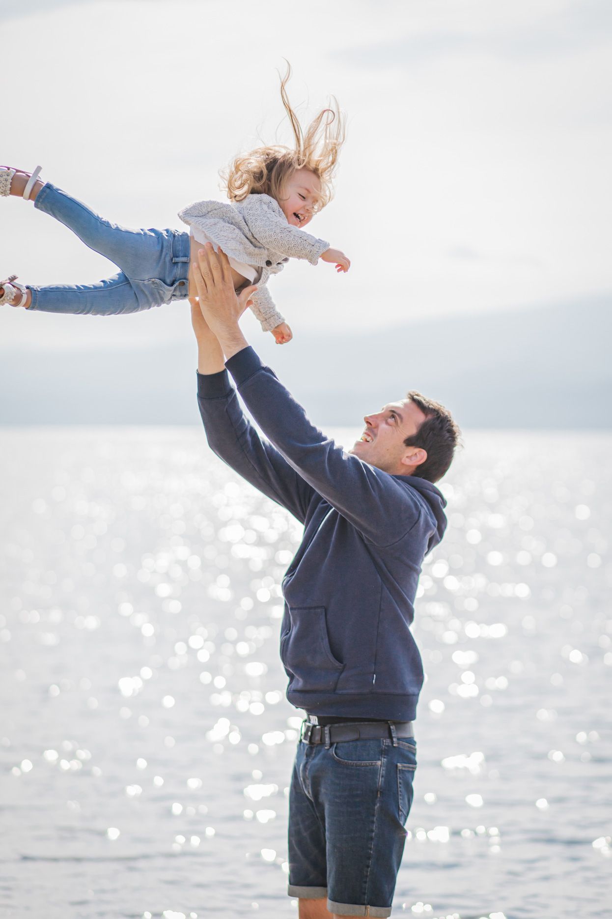 Playful moment captured by water as someone lifts a child high in the air.