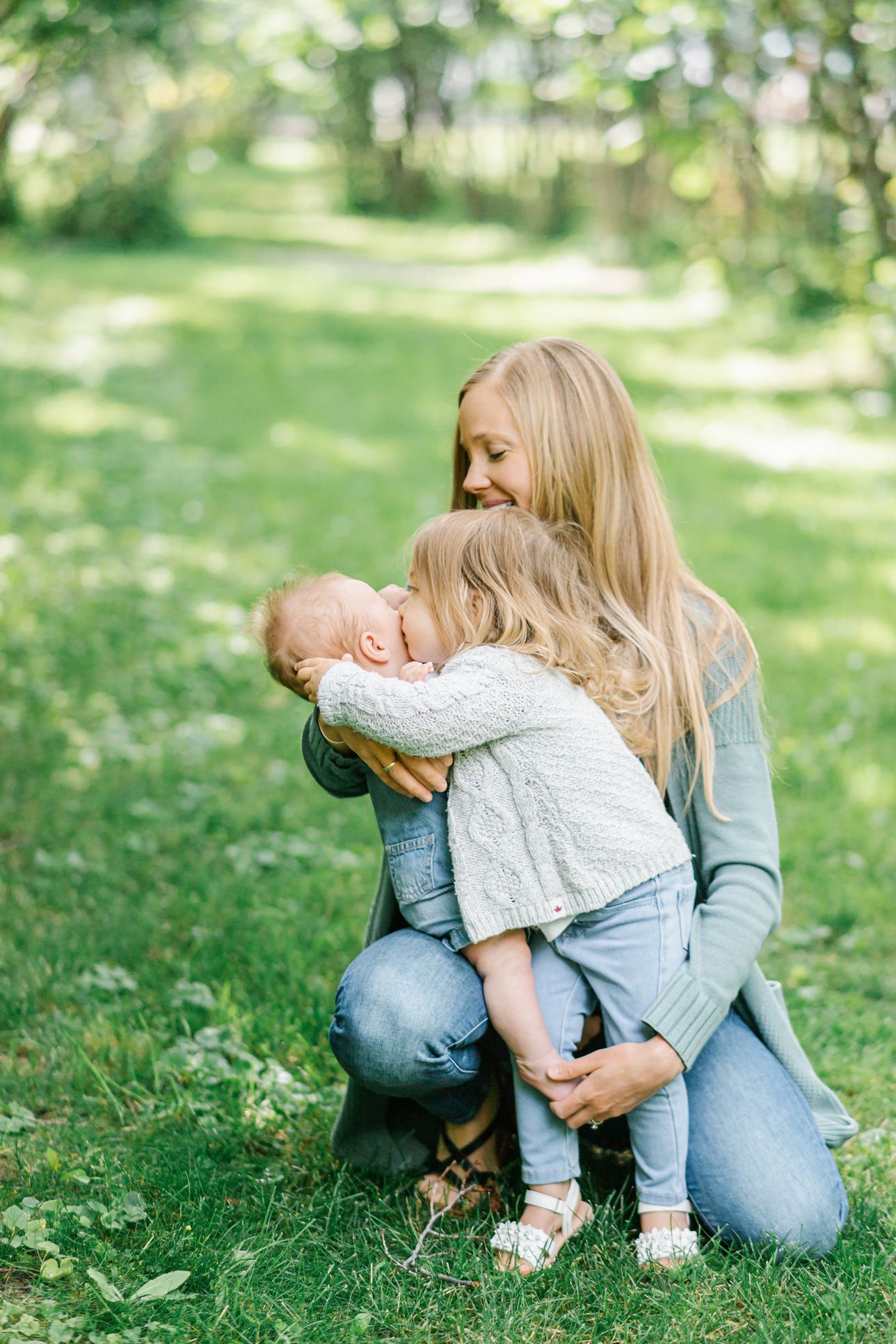 A tender family moment captured in a sunlit garden with gentle embraces.