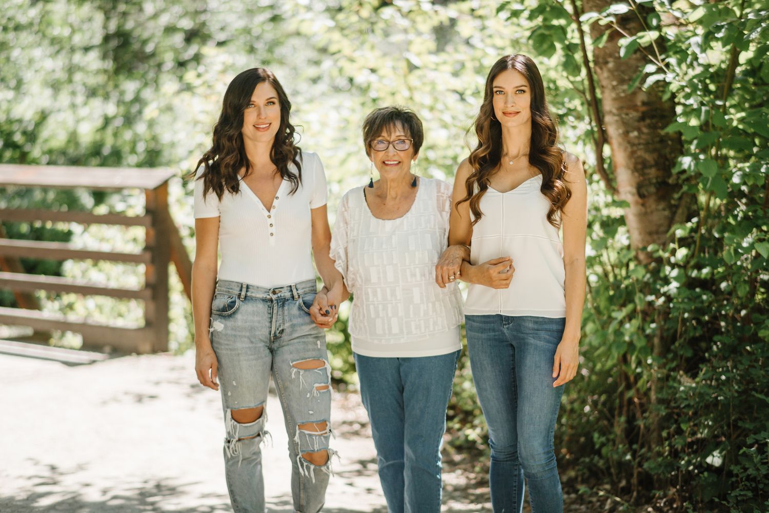 Three generations pose together on a wooden walkway surrounded by lush greenery.