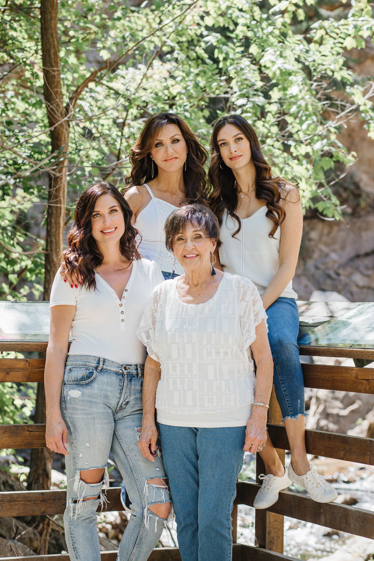 Four generations of family members pose together on a rustic wooden bridge in nature.