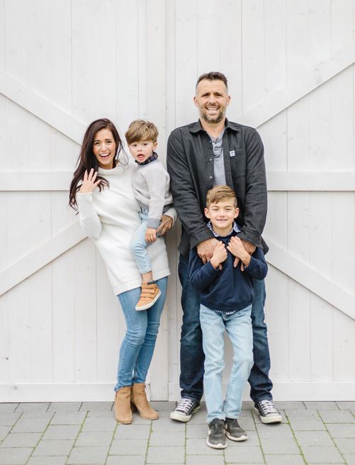 A family poses together against a white barn door background in casual attire.