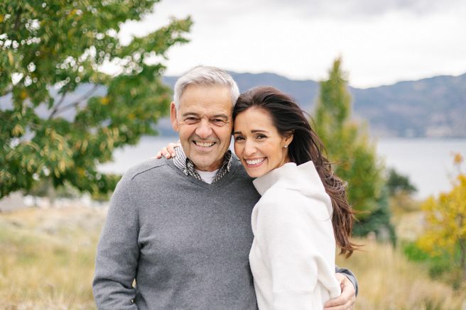 A loving family embraces while standing in a natural outdoor setting with mountains visible.