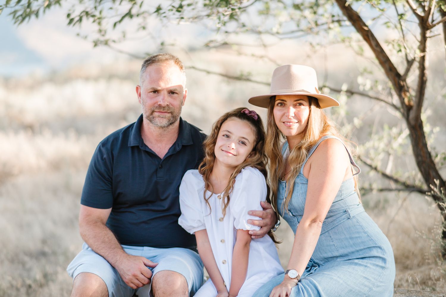 Family members sit together in a sunny field with trees and natural lighting.