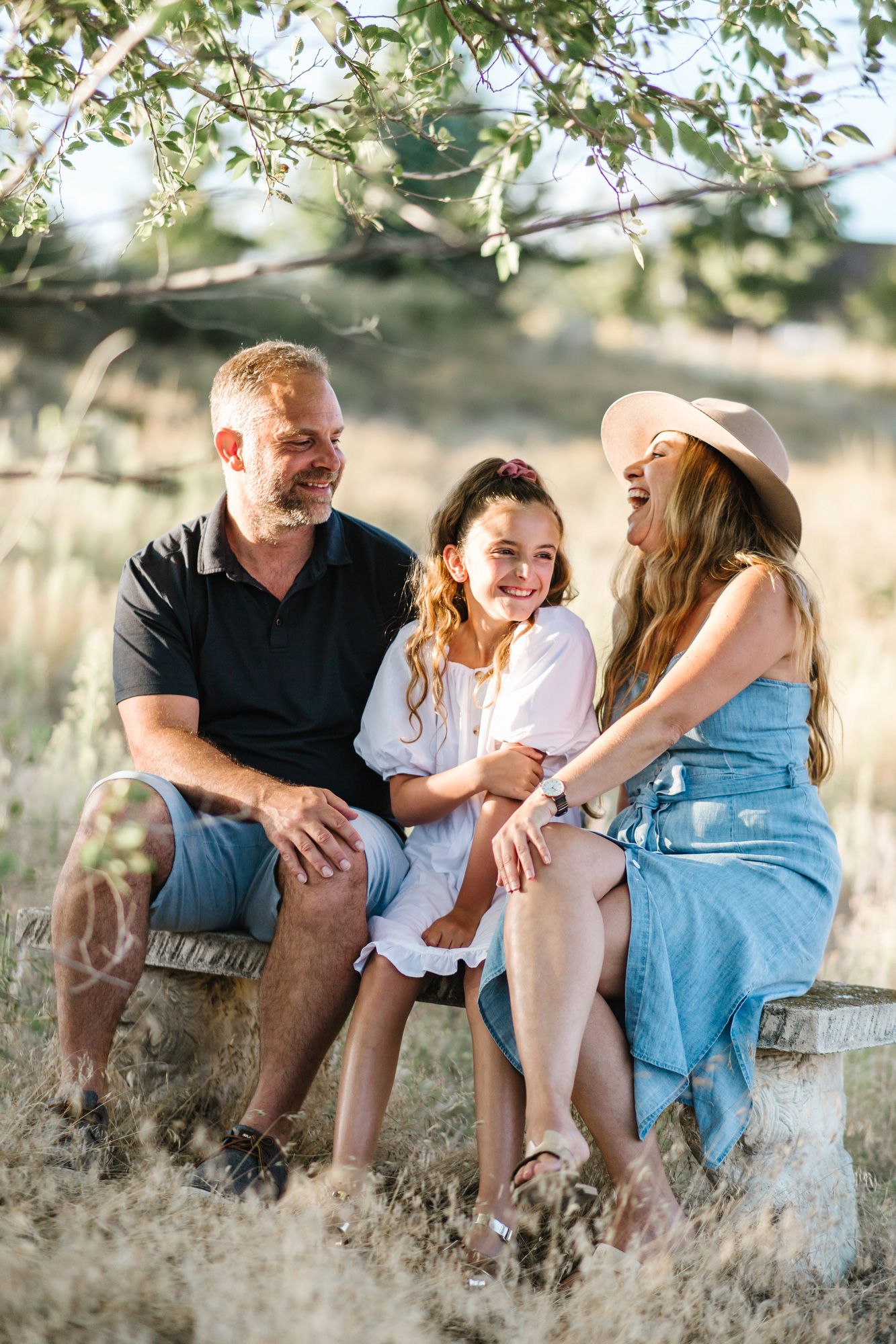 A family shares joyful moments while sitting together in tall grass during golden hour.