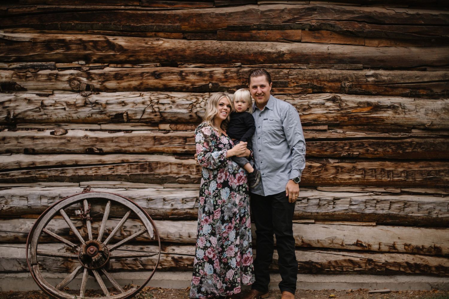 Rustic outdoor portrait session against weathered wooden log cabin walls.