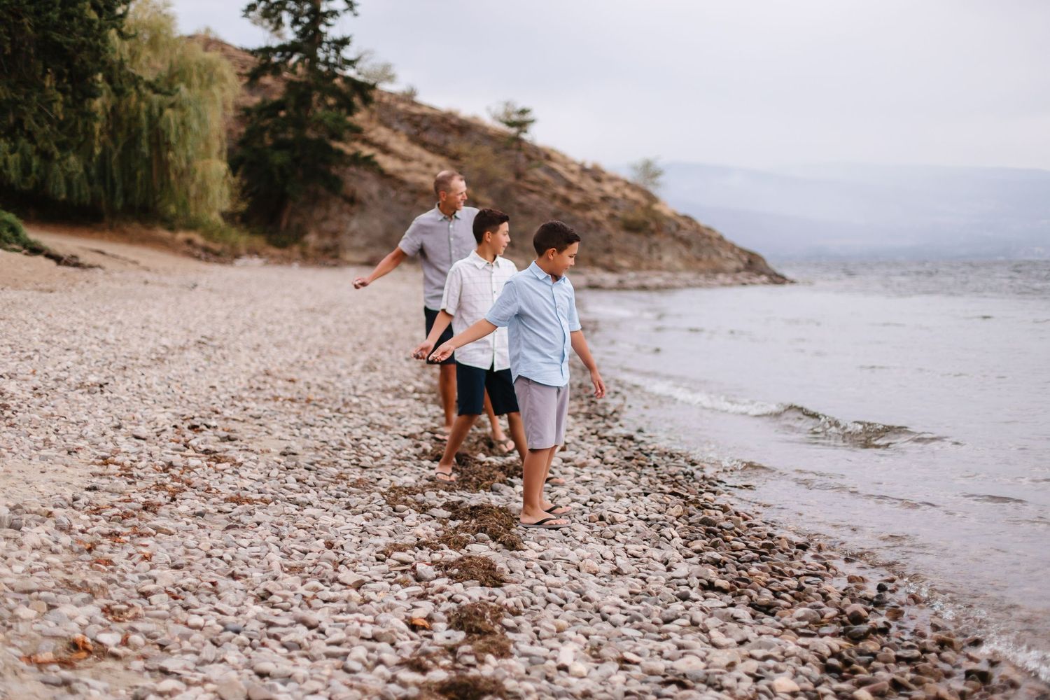 Family walking along a rocky beach shoreline on an overcast day.