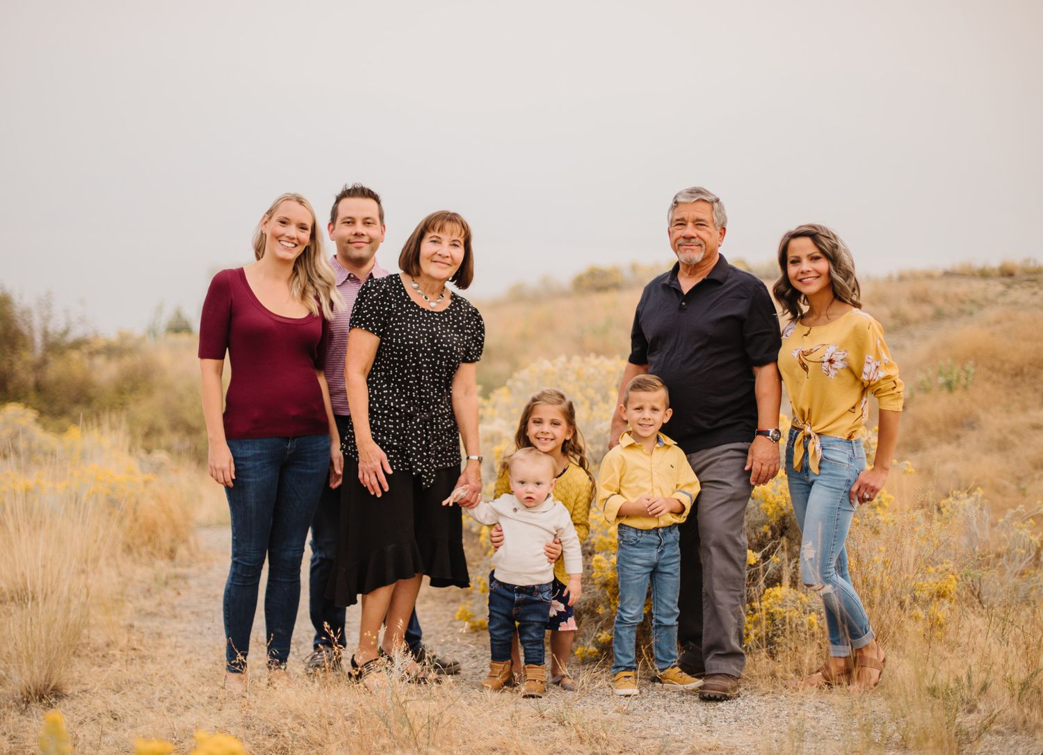 Family group poses together on golden grassy hillside during sunset photoshoot.