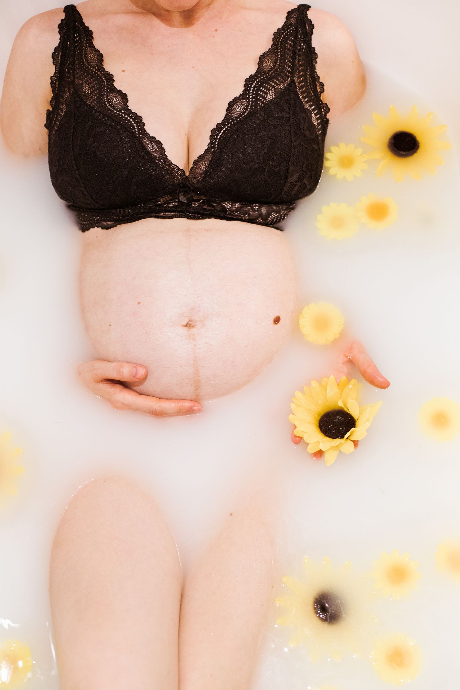 Woman in black lace bralette poses with sunflowers in a light and airy boudoir photoshoot.