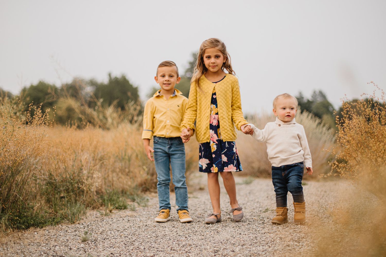 Children walk together on dirt path during golden hour family photoshoot.