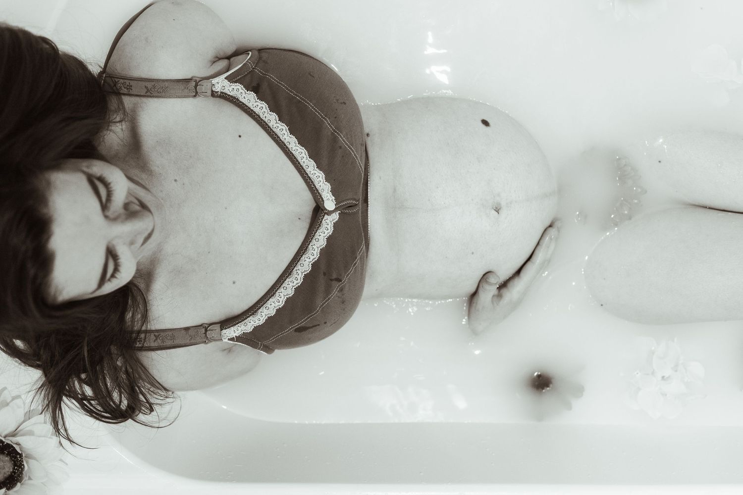 Black and white artistic portrait of woman reclining in bathtub.