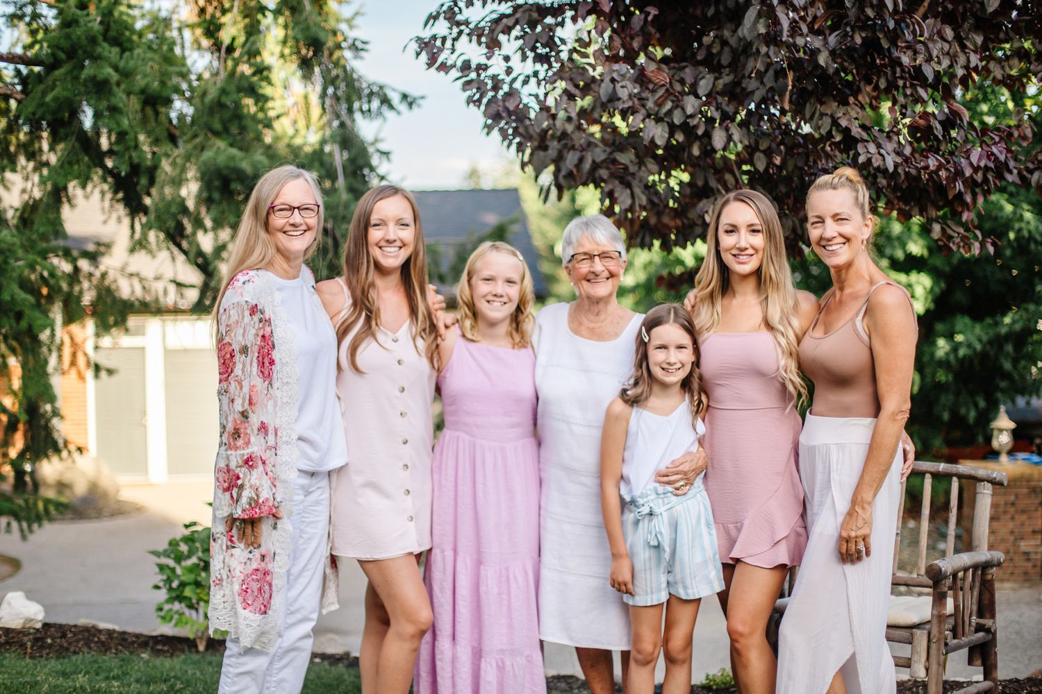 Group wearing coordinated pink and white dresses pose together at outdoor garden party.