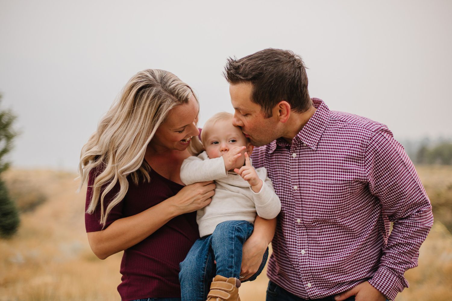 Parents sharing tender moment with baby outdoors during family photo session.