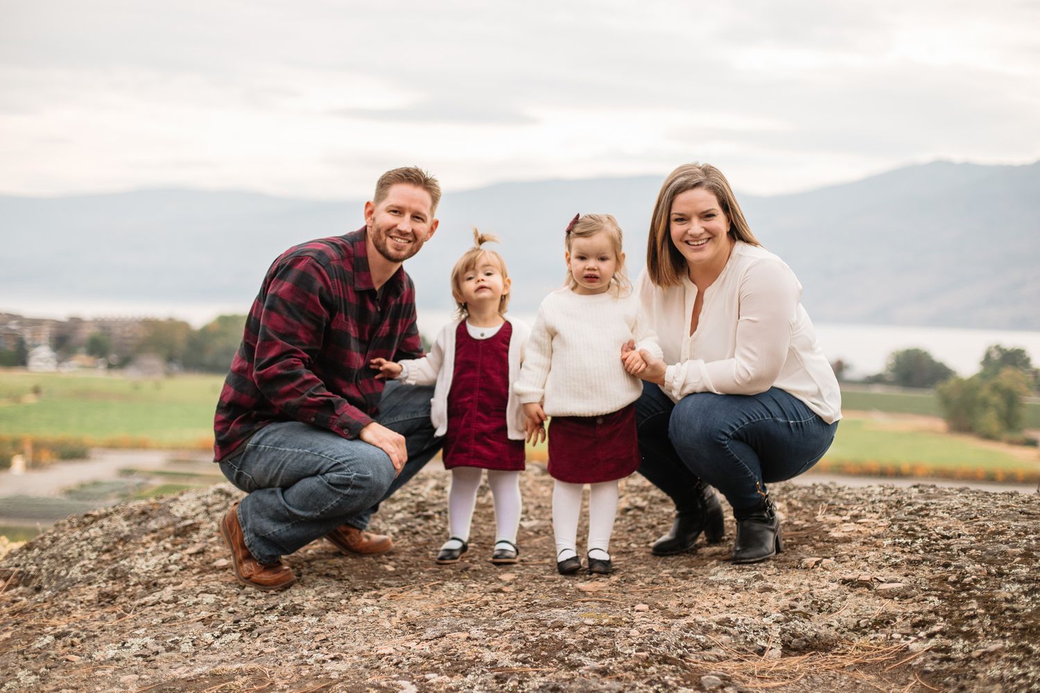 Family of four poses together on rocky overlook with mountain vista in background.