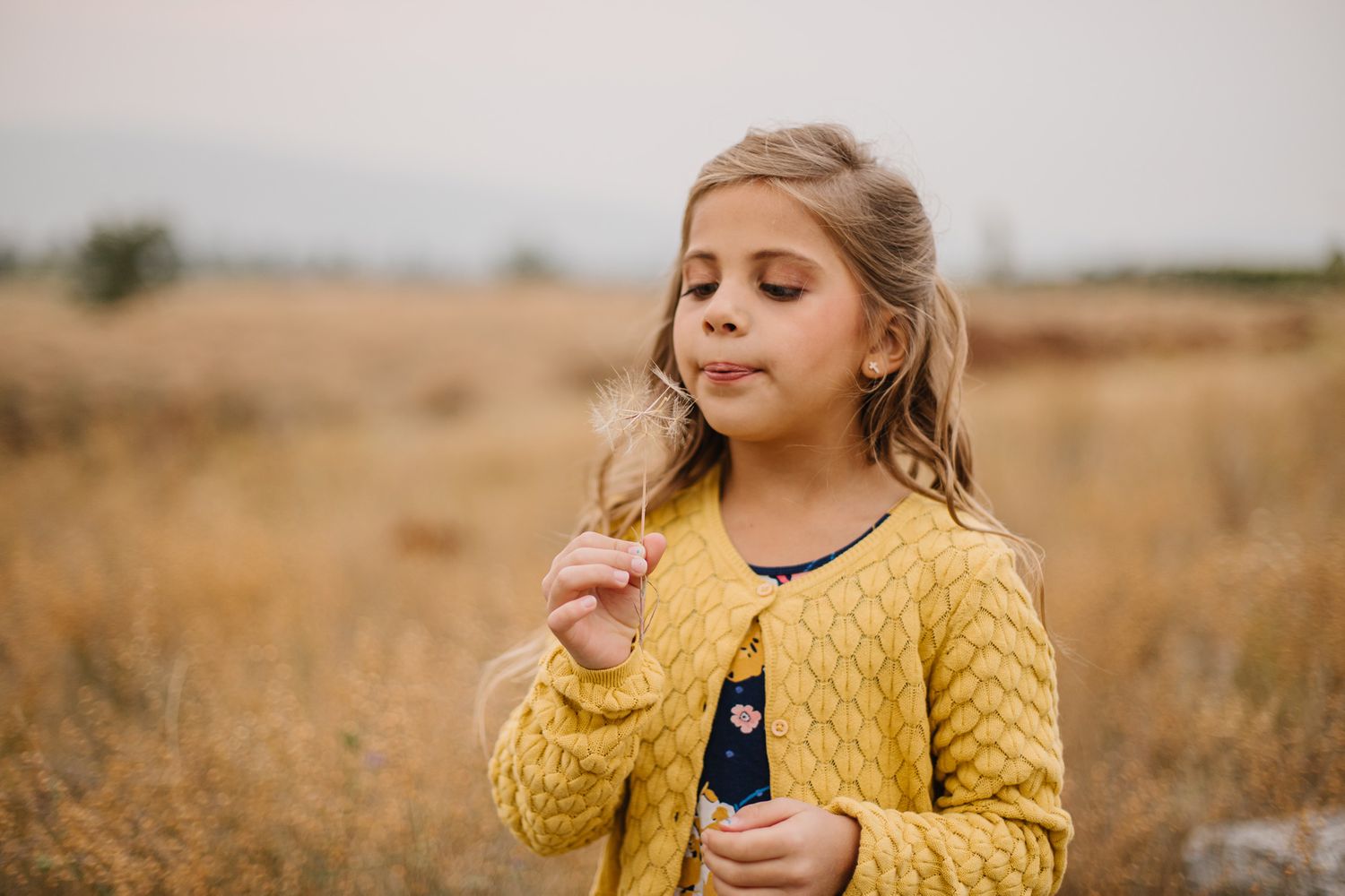 Child in yellow cardigan sweater blowing bubbles in golden field.