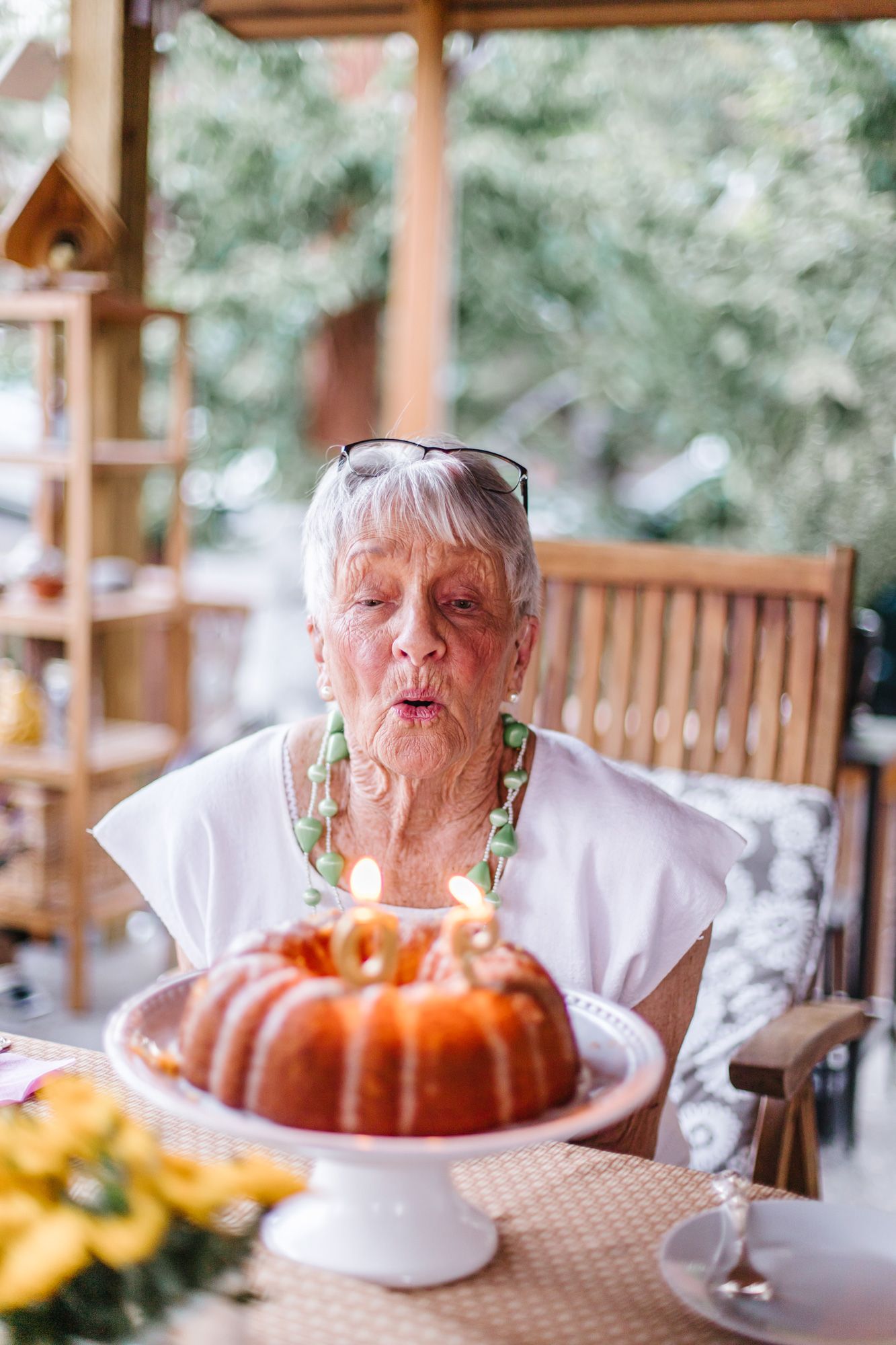 Person blowing out candles on bundt cake at outdoor table setting.