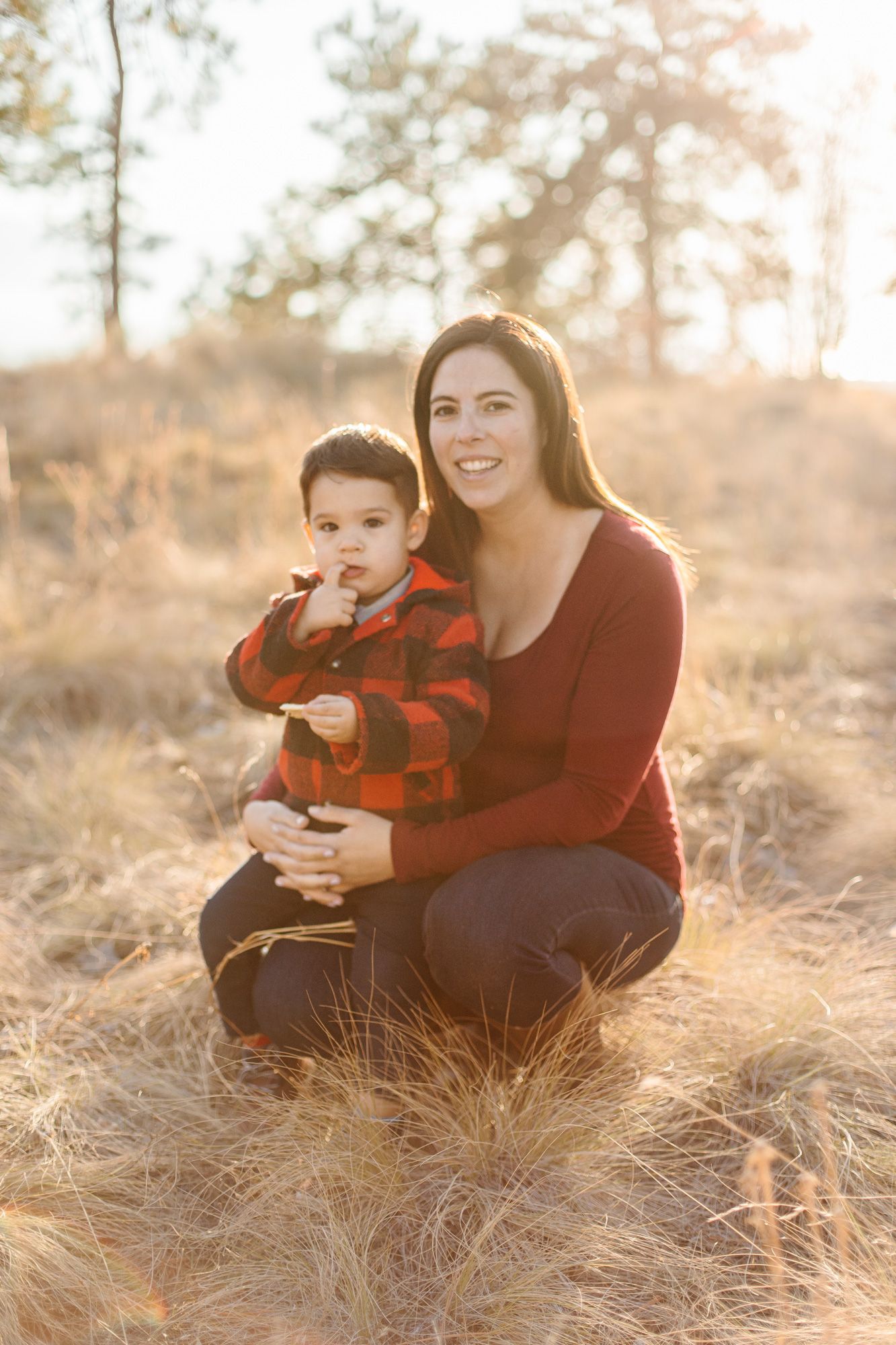 A parent and child in red plaid sit together in golden grass during sunset.