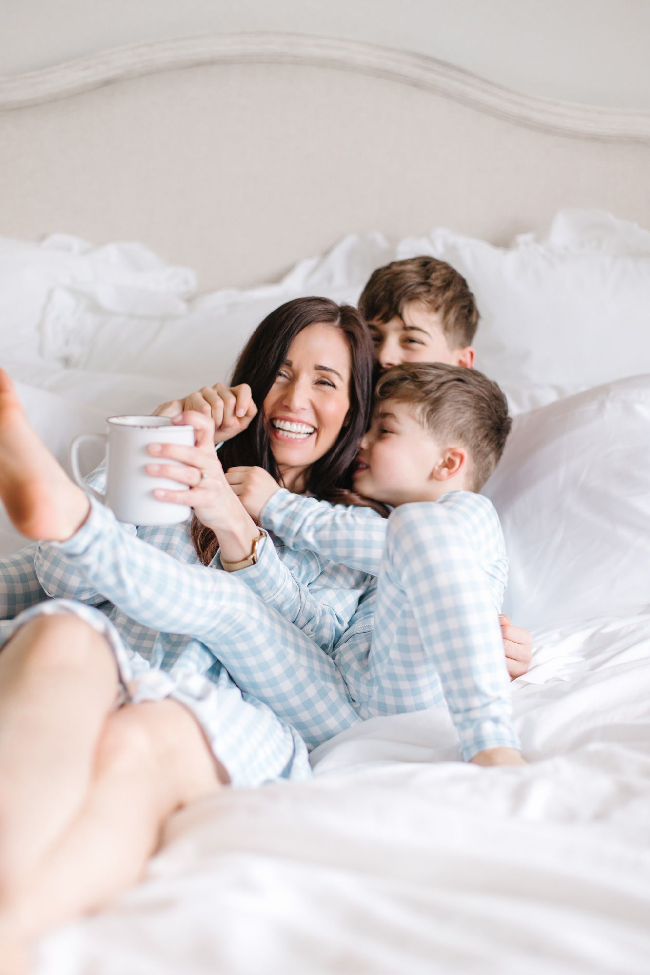 Candid moments of joy captured in soft white bedding while wearing matching blue checkered pajamas.