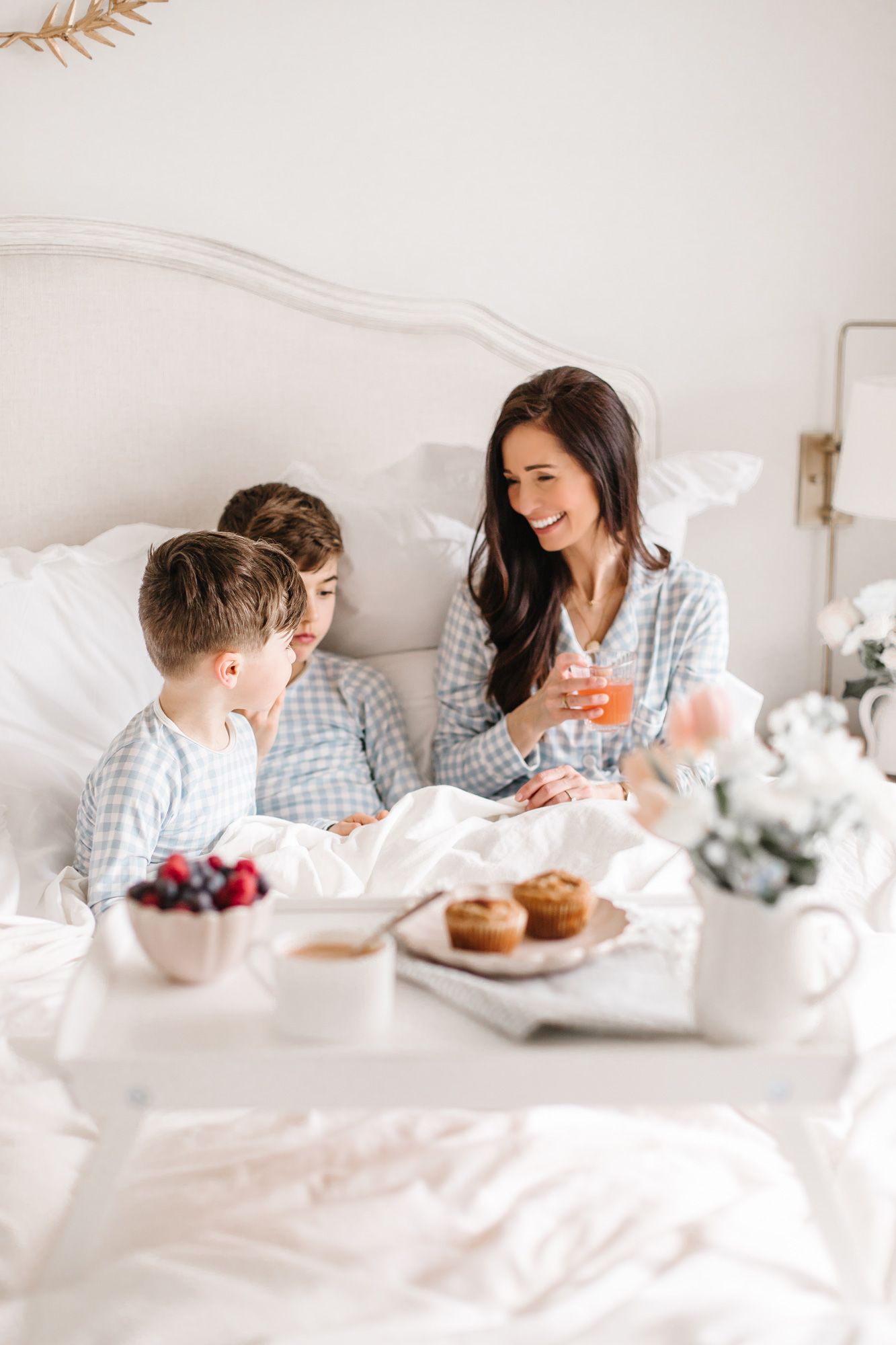 A breakfast in bed scene with pastries and drinks while wearing coordinated blue checkered pajamas.