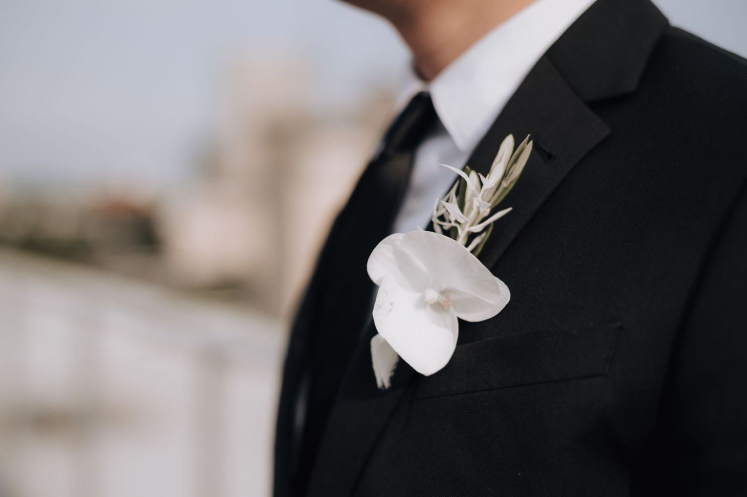 Close-up detail of white orchid boutonniere on black suit lapel.
