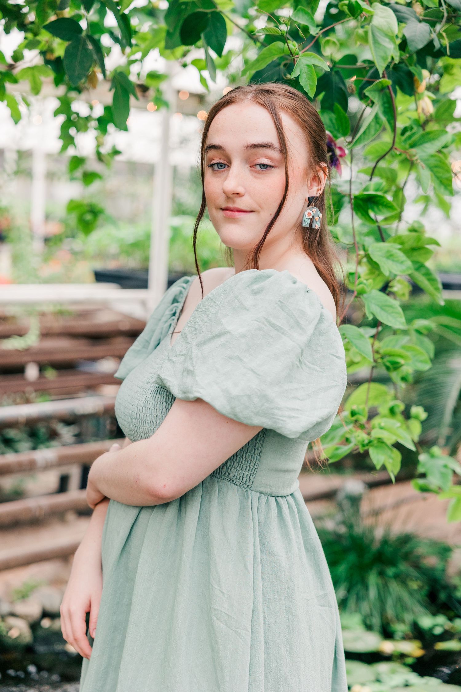 Side portrait in romantic sage dress with puff sleeves against garden greenery.