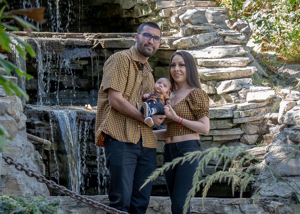 Family of three posing in front of a stone waterfall outdoors.