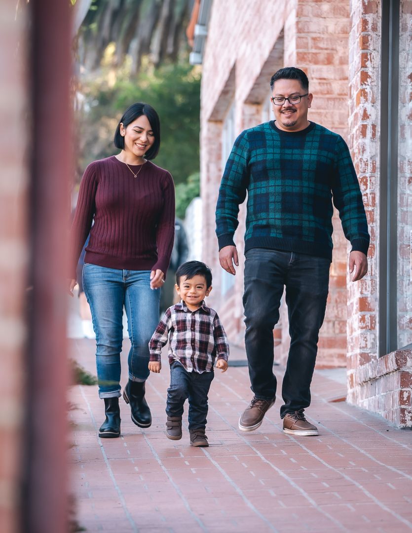 Young Hispanic family walks hand in hand along a charming brick-lined outdoor walkway.