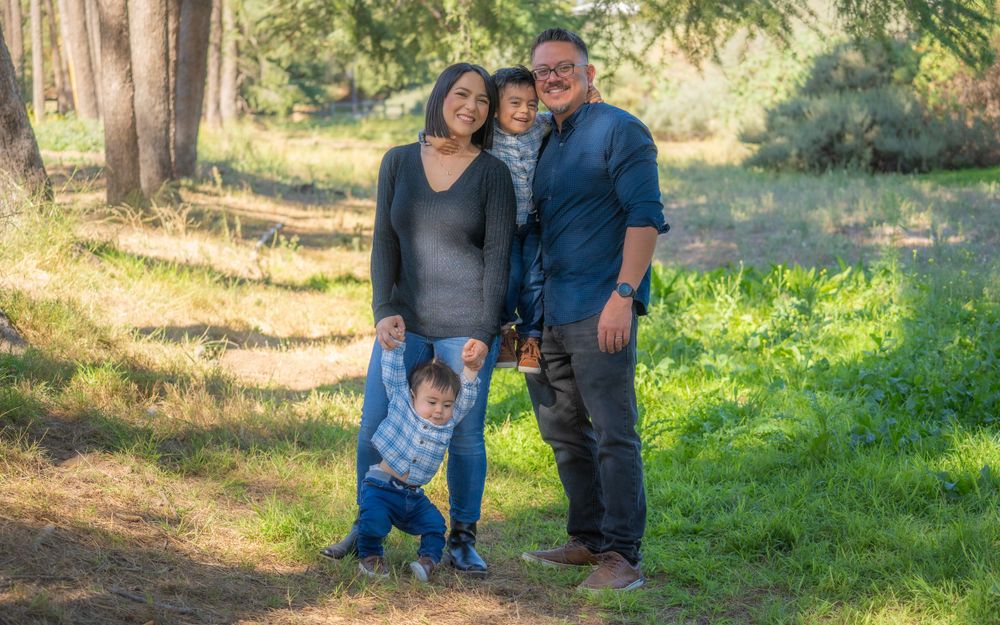 Smiling Asian family with two young boys poses together on a sunlit nature trail path.