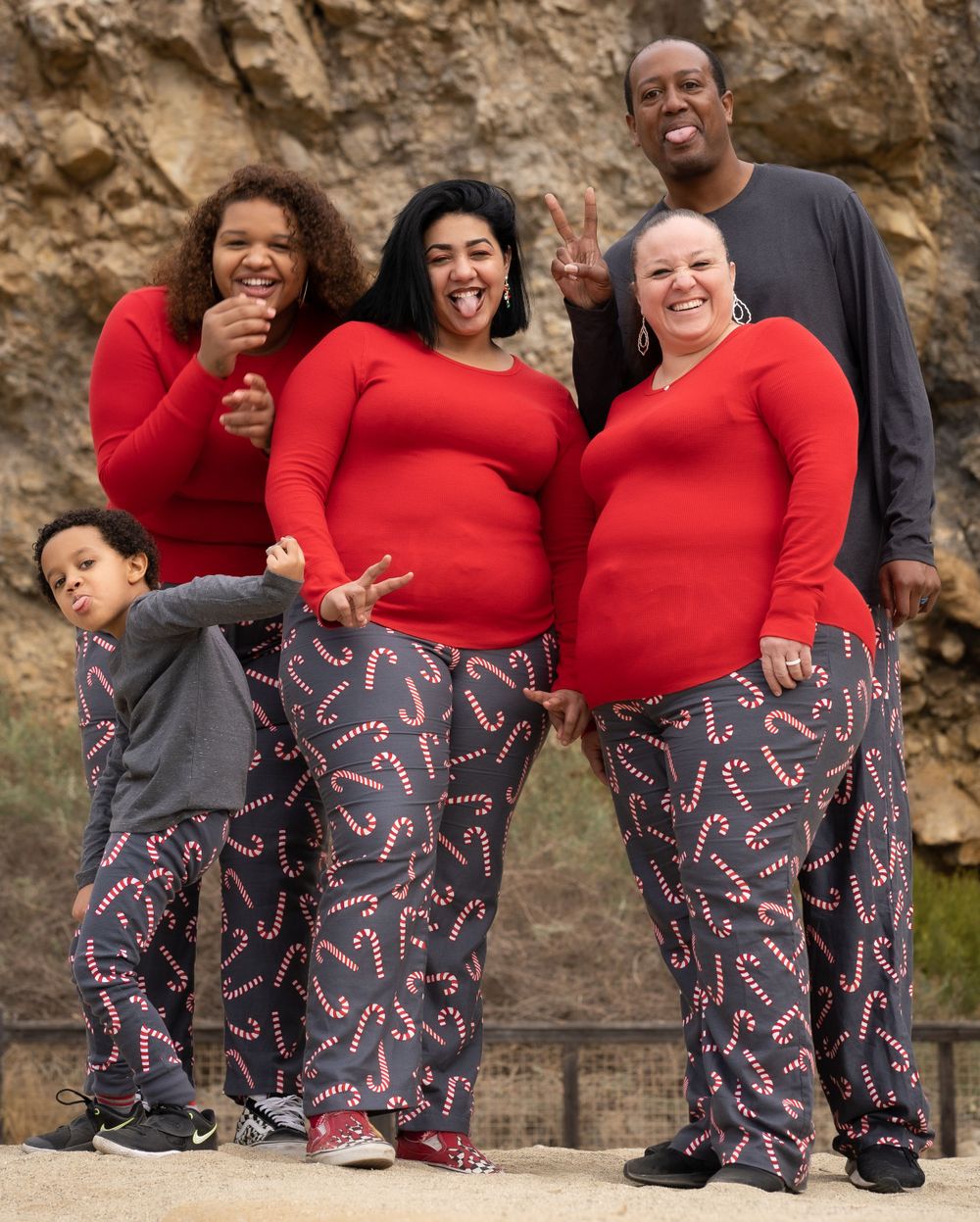 Family of five in matching red and candy cane pajamas posing outdoors.
