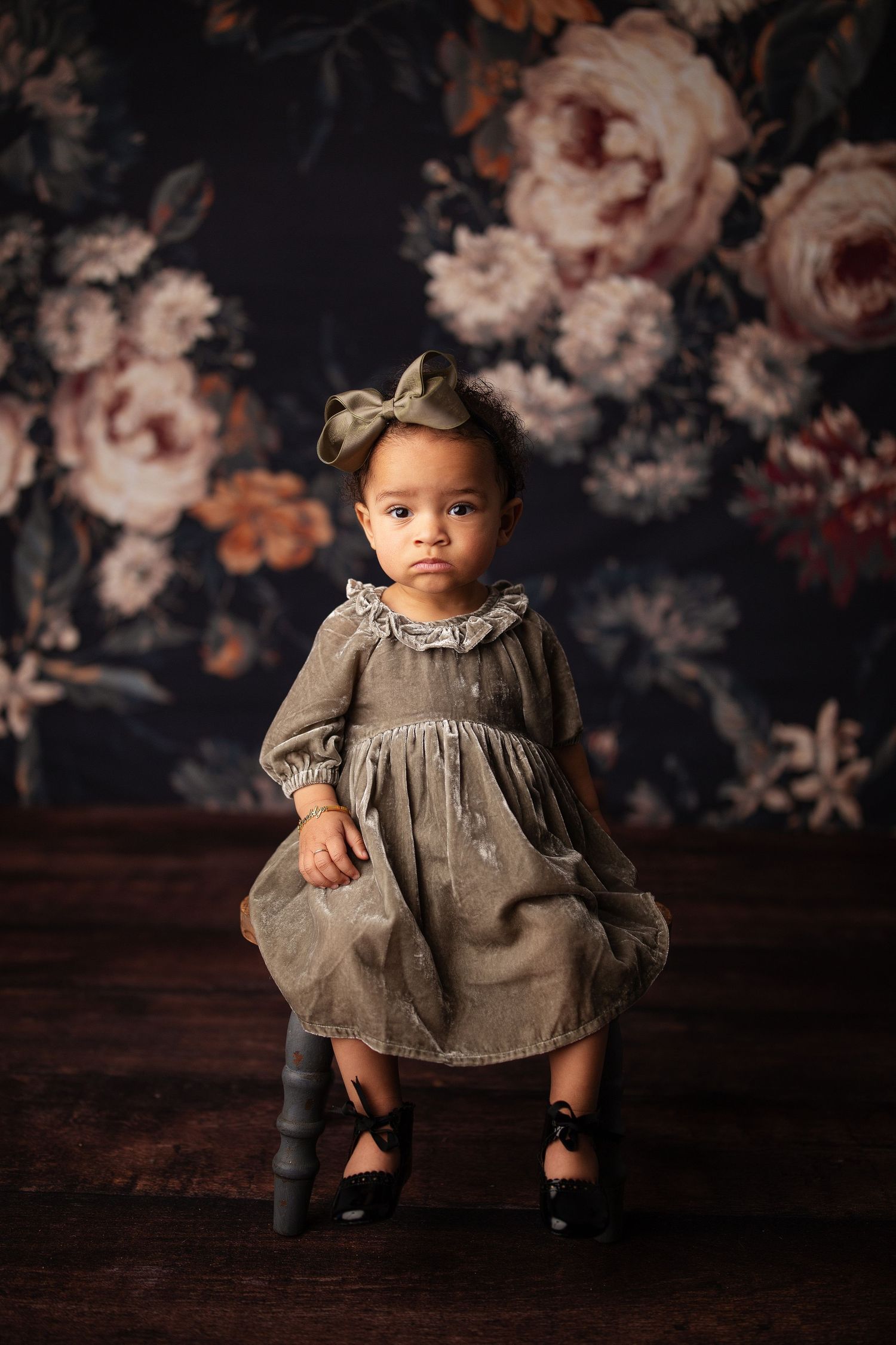 baby girl sitting on bench in front of a floral backdrop at her milestone photography session in Broken Arrow,OK