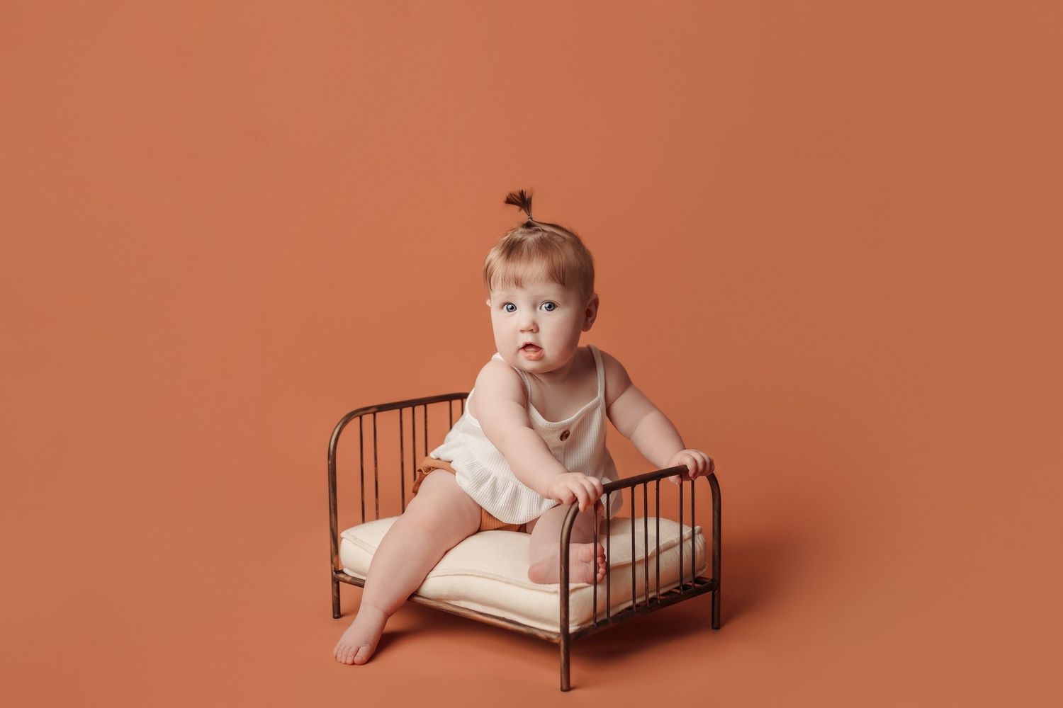 baby girl at her milestone photography session sitting on bed prop