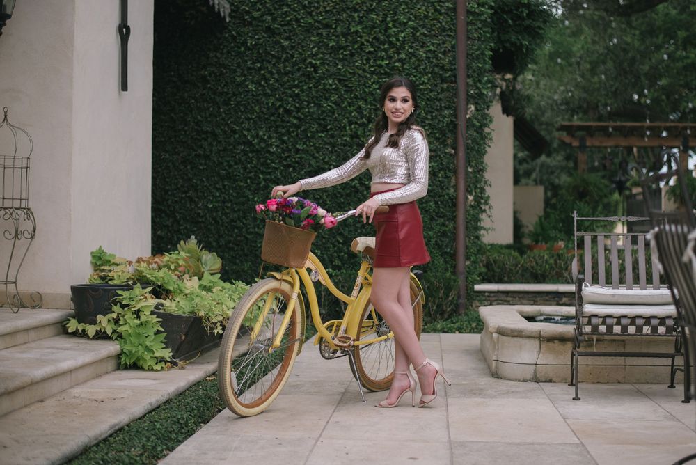 girl holding a bike standing next. girl seating on red couch outside. quinceanera. Casa Polonia. Weslaco, Texas. Wedding