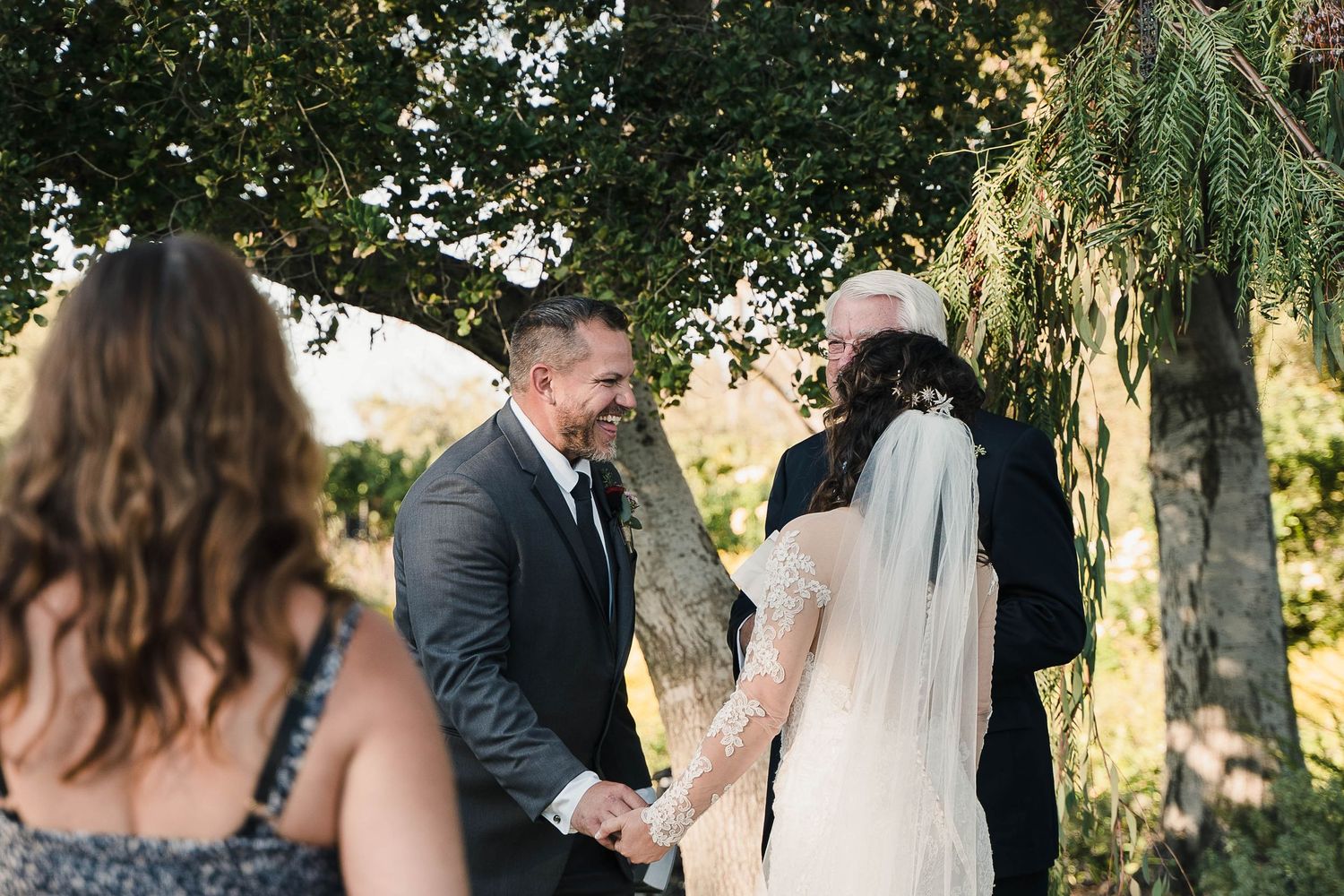 An emotional outdoor wedding ceremony moment under trees with guests looking on.