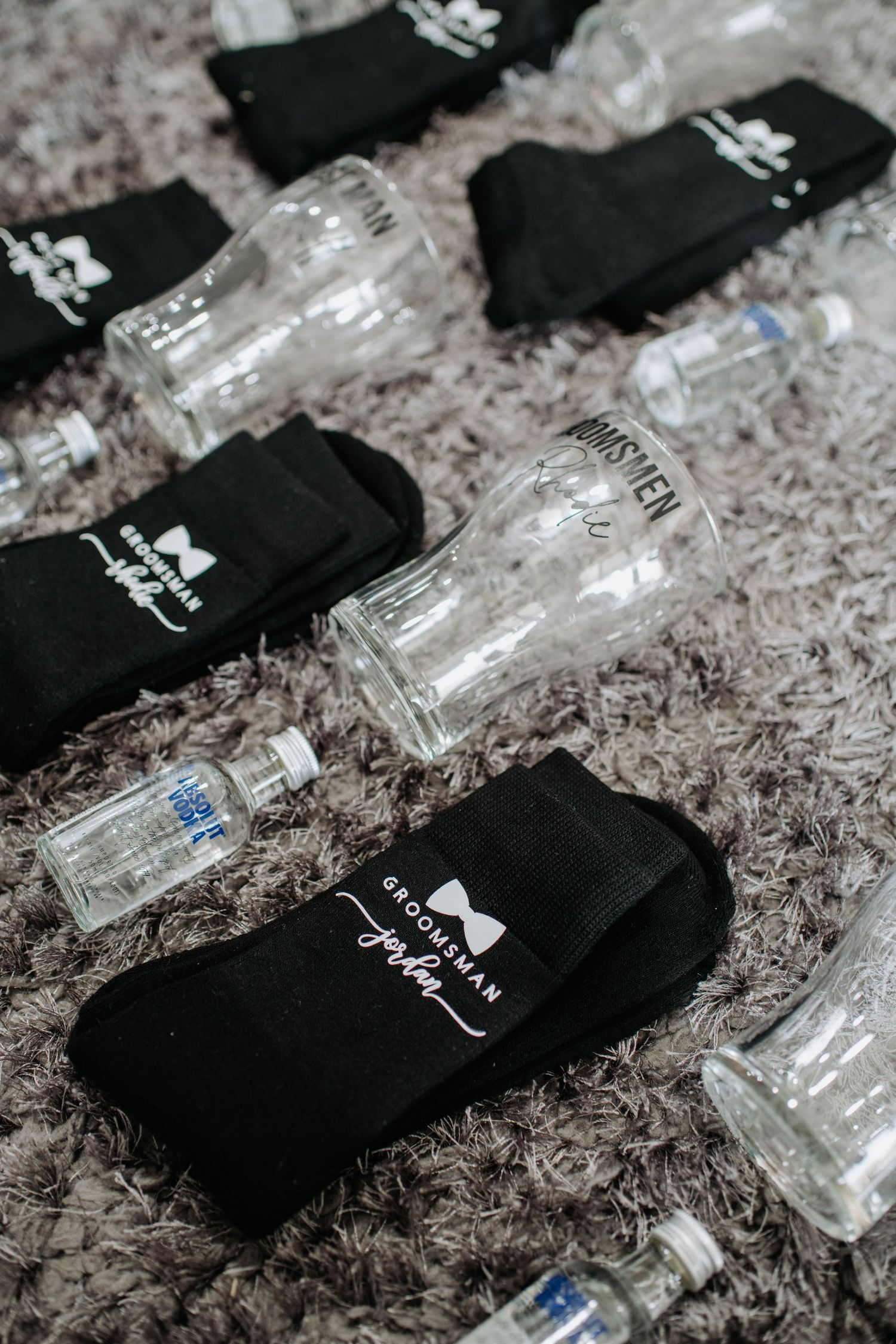 Black wedding socks arranged with miniature vodka bottles on a gray carpet.